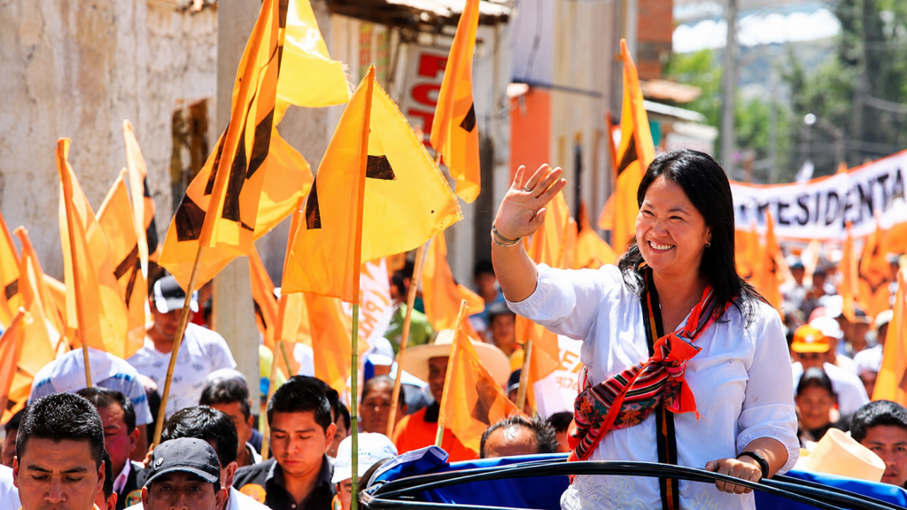 Lideresa política saluda a simpatizantes durante una concentración con banderas naranjas en Perú.