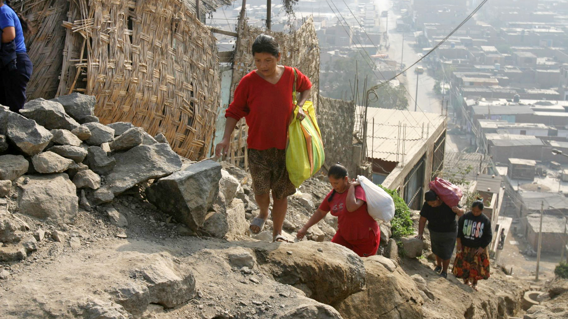 Mujeres suben por una ladera en un asentamiento urbano del Perú, reflejando la pobreza y las brechas sociales.