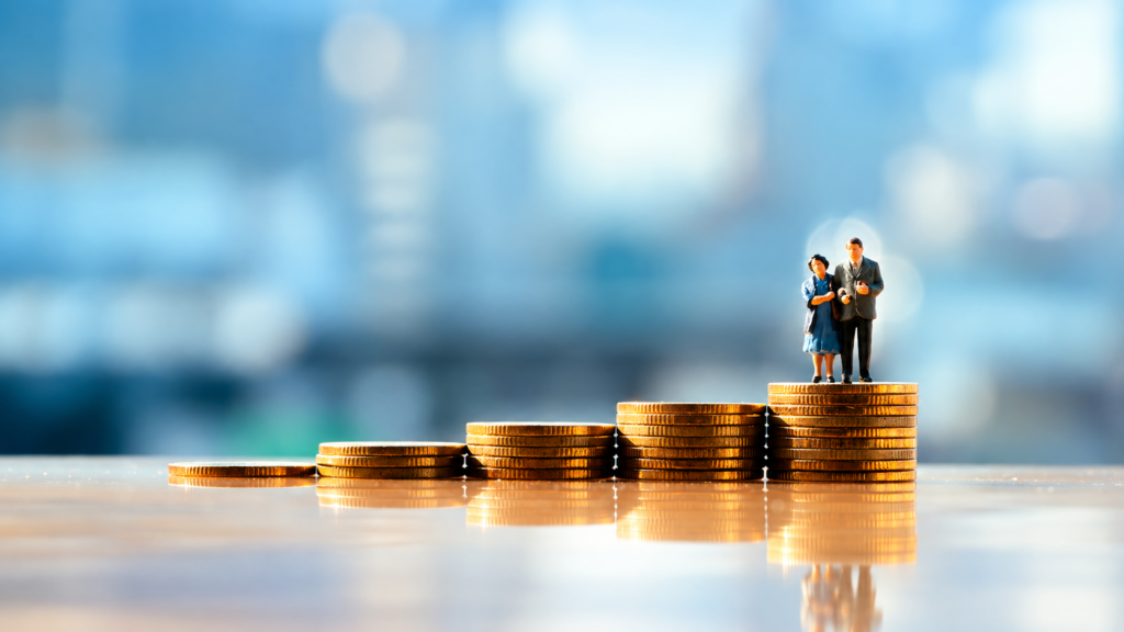 Pareja de adultos mayores sobre pilas de monedas como símbolo de ahorro, pensiones y seguridad financiera.